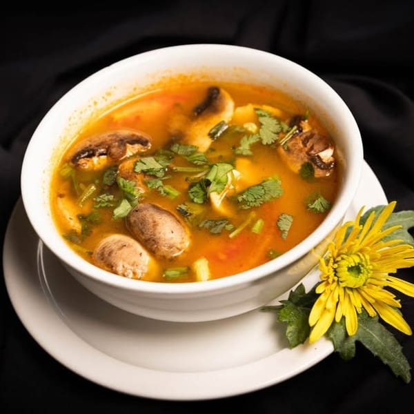 A white bowl of mushroom soup with cilantro, garnished with a yellow flower on a black cloth.