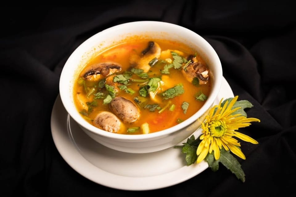 A white bowl of mushroom soup with cilantro, garnished with a yellow flower on a black cloth.