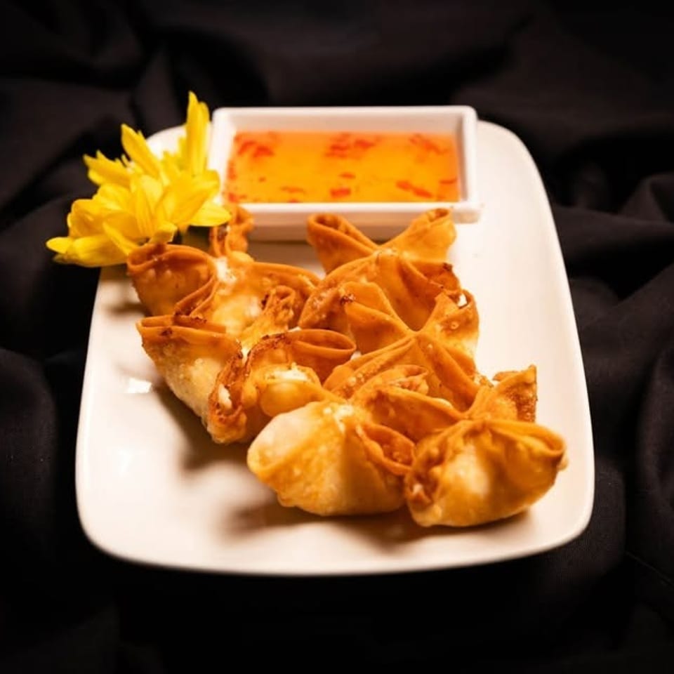 Crispy crab rangoons with sweet chili dipping sauce and a yellow flower on a white plate.
