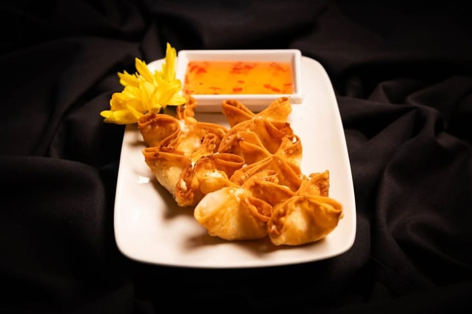 Crispy crab rangoons with sweet chili dipping sauce and a yellow flower on a white plate.