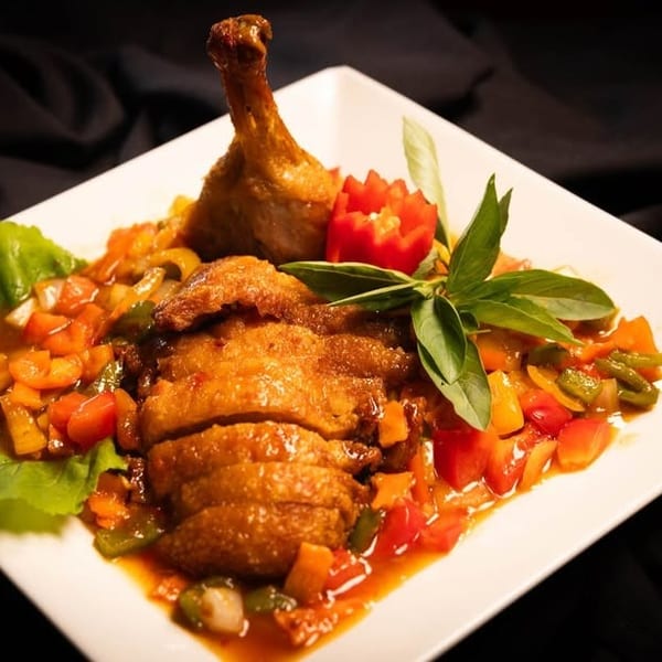 Crispy duck with colorful stir-fried vegetables and sauce, garnished with basil and carved tomato.